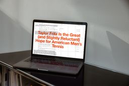 A photo of a laptop on which Caira Conner's portfolio is open. A table of articles with two open, behind, large orange text of an article title reads Taylor Fritz is the Great (and Slightly Reluctant) Hope for American Men's Tennis